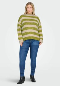 Gestreepte trui in groen en beige, ontspannen pasvorm, gebreide textuur. Gecombineerd met blauwe jeans en zwarte enkelboots.