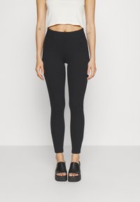 Fekete, magas derekú leggings, rugalmas anyagból, sima textúrával és szoros illeszkedéssel, fekete, vastag talpú csúszó szandálokkal párosítva.