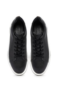 Un paio di sneakers nere in pelle texture con lacci neri e suole in gomma bianca, viste dall'alto su uno sfondo bianco.
