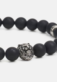 Sorte perlearmbånd med glatte matte perler og et sølv lionhoved som midtpunkt med detaljeret gravering.
