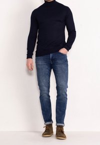 Granatowy sweter z golfem, dopasowany, zestawiony ze średnio wypranymi dżinsami. Brązowe buty sznurowane o lekko surowej fakturze. Prosty, nowoczesny design.