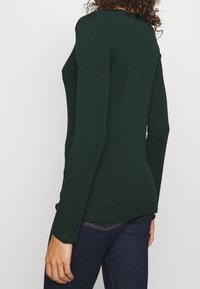 Mörkgrön långärmad tröja med en åtsittande design, tillverkad av mjukt material, med rund halsringning och slät textur.