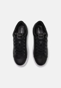 Black leather sneakers with a smooth texture, round toe, white rubber sole, and black laces. Features branding on the tongue.