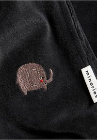 Svart tyg med en mjuk textur som har en liten broderad brun elefantdesign med en röd accent på snabeln, tillsammans med en vit etikett.