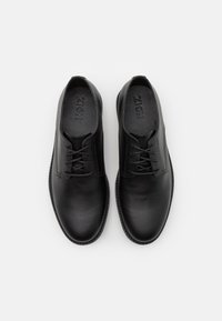 Scarpe in pelle nera con una texture liscia, punta rotonda e lacci sottili. Presentano un sottile dettaglio di cucitura lungo i bordi.