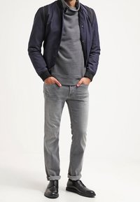 Laivastonsininen pommikäsittelytakki harmaan poolopaidan, harmaiden farkkujen ja mustien nahkakenkien päällä. Pehmeät pinnat, joissa on kontrastia kauluksessa ja rento istuvuus.