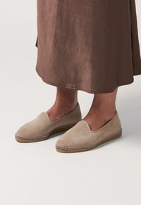 Beige suede slip-on shoes with a woven jute sole, featuring a low profile, smooth texture, and simple design.