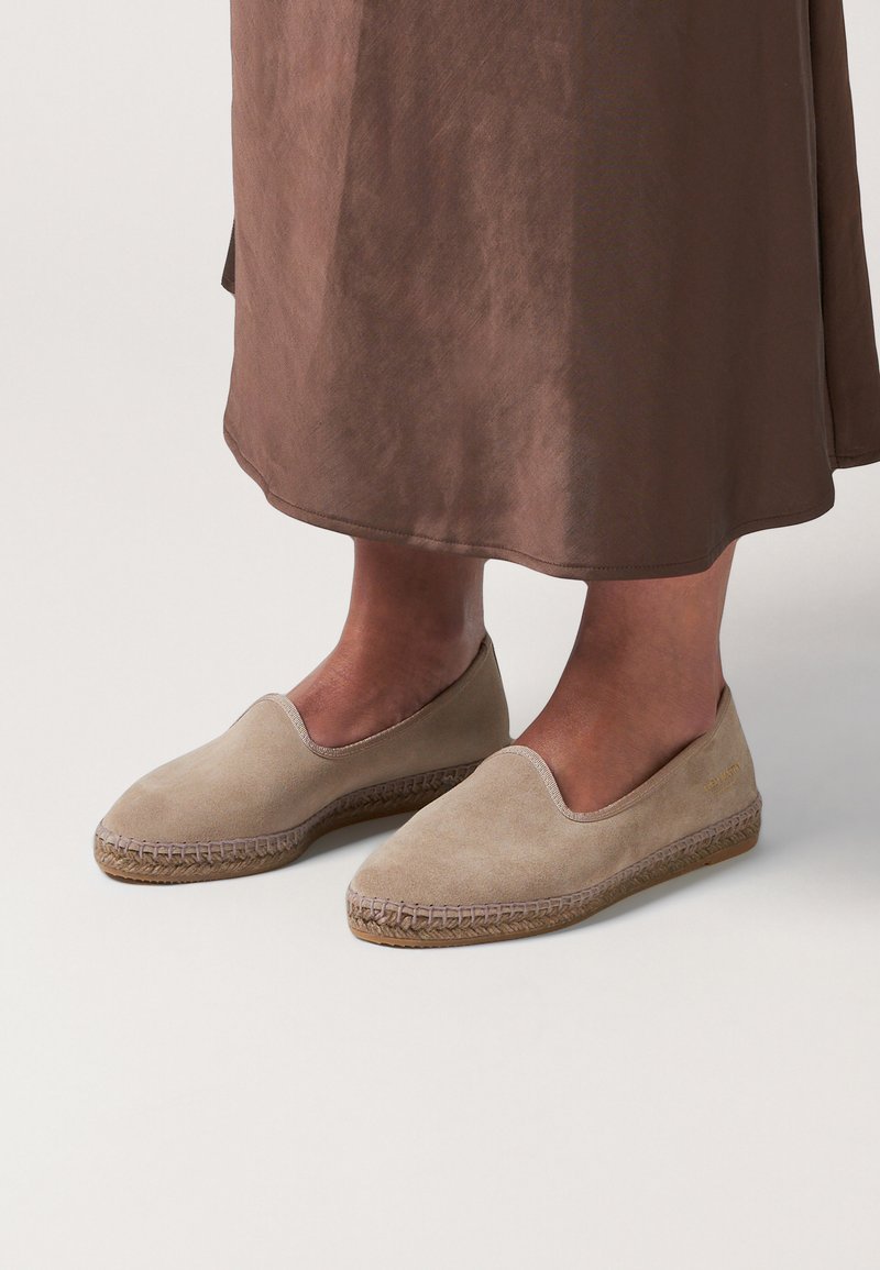Beige Wildleder-Slipper mit einer gewebten Jutesohle, niedriger Profilhöhe, glatter Textur und schlichter Gestaltung.