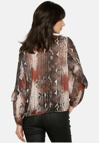 Schlangenmuster-Bluse in Brauntönen, Beige und Schwarz; verfügt über lange, voluminous Ärmel und ein fließendes Design mit einer glatten Textur.
