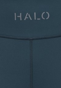 Close-up af mørkeblåt stof med synlige syninger og ordet "HALO" trykt med lyse bogstaver nær toppen i midten.