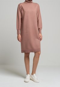Robe en maille rose pâle avec col montant, manches longues et poignets et ourlet côtelés. Portée avec des baskets blanches. Fini lisse et texturé.
