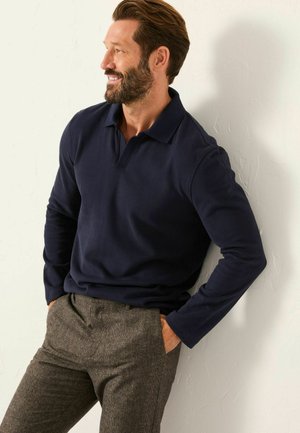 Marineblaues Langarm-Polohemd aus weichem Stoff, kombiniert mit grauen karierten Hosen. Es bietet eine lockere Passform und ein klassisches Kragen-Detail.
