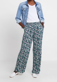 Spodnie w kwiaty o szerokich nogawkach w ciemnozielonym kolorze z białymi i różowymi kwiatami. Połączone z lekką dżinsową kurtką i białym T-shirtem.