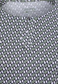 Patterned top featuring a geometric design in green, black, and white, with a button placket and 'eco-friendly' label in the collar.