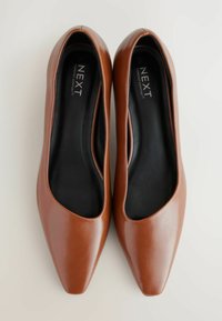 Braune spitze Absatzschuhe aus Kunstleder mit glänzender Oberfläche, die eine glatte Textur und eine schwarze gepolsterte Innensohle aufweisen. Der Markenname ist sichtbar im Inneren.