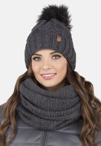 Bonnet en tricot gris foncé avec un pompon en fourrure sur le dessus et un patch en cuir. Accompagné d'une écharpe cowl en tricot épais assortie.