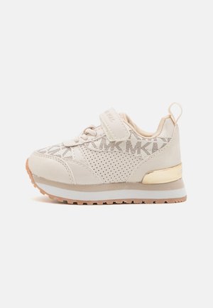 Baskets de sport beige avec un dessus en mesh texturé, des côtés perforés, une sangle Velcro et un accent doré sur le talon. Semelle en caoutchouc conçue pour la traction.