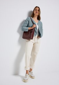 Cardigan blu chiaro e textured sopra una maglia grigia, abbinato a pantaloni color crema e sneakers grigie. È inclusa una borsa a tracolla in pelle marrone.