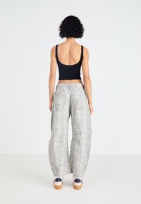Zwart geribbelde tanktop en losse, gepatterneerde grijze slangenprintbroek met zakken en cropped lengte, gestyled met lichte schoenen.