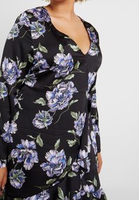 Svart klänning med långa ärmar, med en djup V-ringning. Mönstrad med stora blå och gröna blommor. Slät tyg med en lätt lyster.