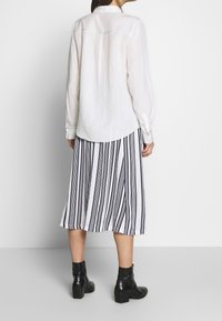 White long-sleeve shirt with a collar, paired with a black and white striped midi skirt and ankle boots, featuring a textured finish.