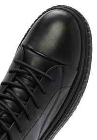 Sneaker in pelle nera con una superficie liscia, punta rotonda, cuciture rinforzate e lacci neri piatti; presenta una suola in gomma testurizzata.