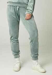 Samt-Jogginghosen in sanftem Mintgrün, mit elastischem Bund und Kordelzug, tapered Beinen und gerippten Knöcheln. Kombiniert mit weißen Sneakers.