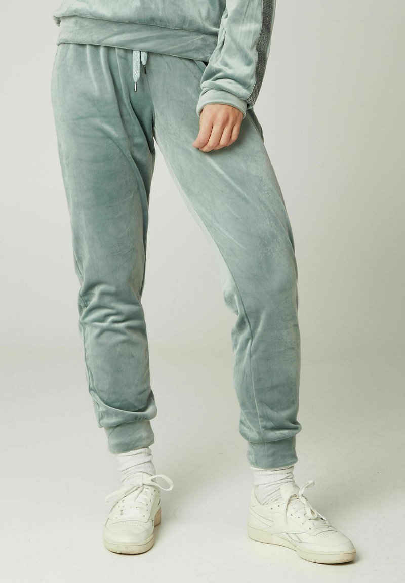 Samt-Jogginghosen in sanftem Mintgrün, mit elastischem Bund und Kordelzug, tapered Beinen und gerippten Knöcheln. Kombiniert mit weißen Sneakers.