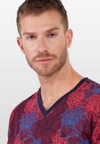 T-Shirt mit V-Ausschnitt in Dunkelrot mit blauem Blumenmuster, ausgestattet mit kurzen Ärmeln und einem marineblauen Halsabschlus. Weicher, strukturierter Stoff mit dezentem Glanz.