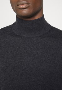 Pull à col roulé gris foncé en tissu côtelé, avec un col haut et une texture lisse, présentant une silhouette ajustée.