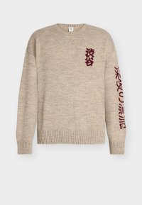 Beige strikkegenser med ribbet kant og mansjetter. Har burgunder grafisk tekst på foran og på ermet. Laget av mykt, teksturert garn.