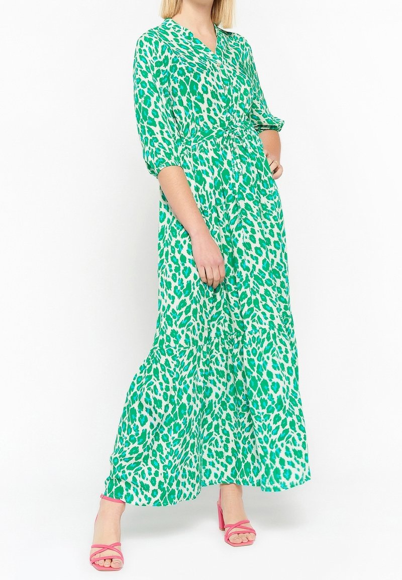 Grön maxiklänning med leopardmönster, med V-ringning, 3/4-långa ärmar och midjeband; parat med rosa klacksandaler.