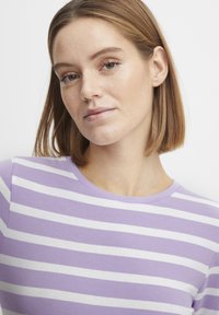 Lila och vit randig t-shirt med rund hals, korta ärmar, mjukt tyg och en figurnära design. Inga ytterligare mönster eller accenter.