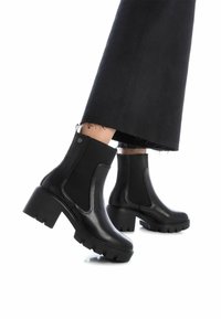 Botas negras hasta el tobillo con un tacón grueso, hechas de cuero suave y tejido elástico. Presentan costuras reforzadas y una suela texturizada para mayor agarre.