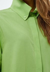 Camicia verde colletto realizzata in tessuto liscia. Presenta una chiusura a bottoni e dettagli di cucitura discreti, con una vestibilità comoda.