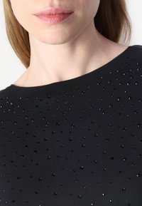 Black top featuring a smooth texture, adorned with shiny black rhinestones in various sizes, highlighting a modern, understated design.