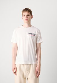 Hvid bomulds t-shirt med rund halsudskæring og korte ærmer, med marineblå og rød broderi der står "GANT 1949."