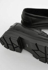 Bottes en cuir noir avec un bout rond, un design à cheville haute et une semelle en caoutchouc épaisse et texturée avec un motif de relief audacieux.