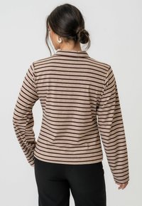 Dugih rukava majica od svijetlosmeđeg materijala s tamnosmeđim horizontalnim prugama. Ima jednostavan ovratnik i uski kroj.