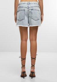 Svijetloplave traper šortse s необрезанím rubom, s dvije stražnje džepove, uparenim s crnim sandalama na visoku potpeticu s remenčićima.