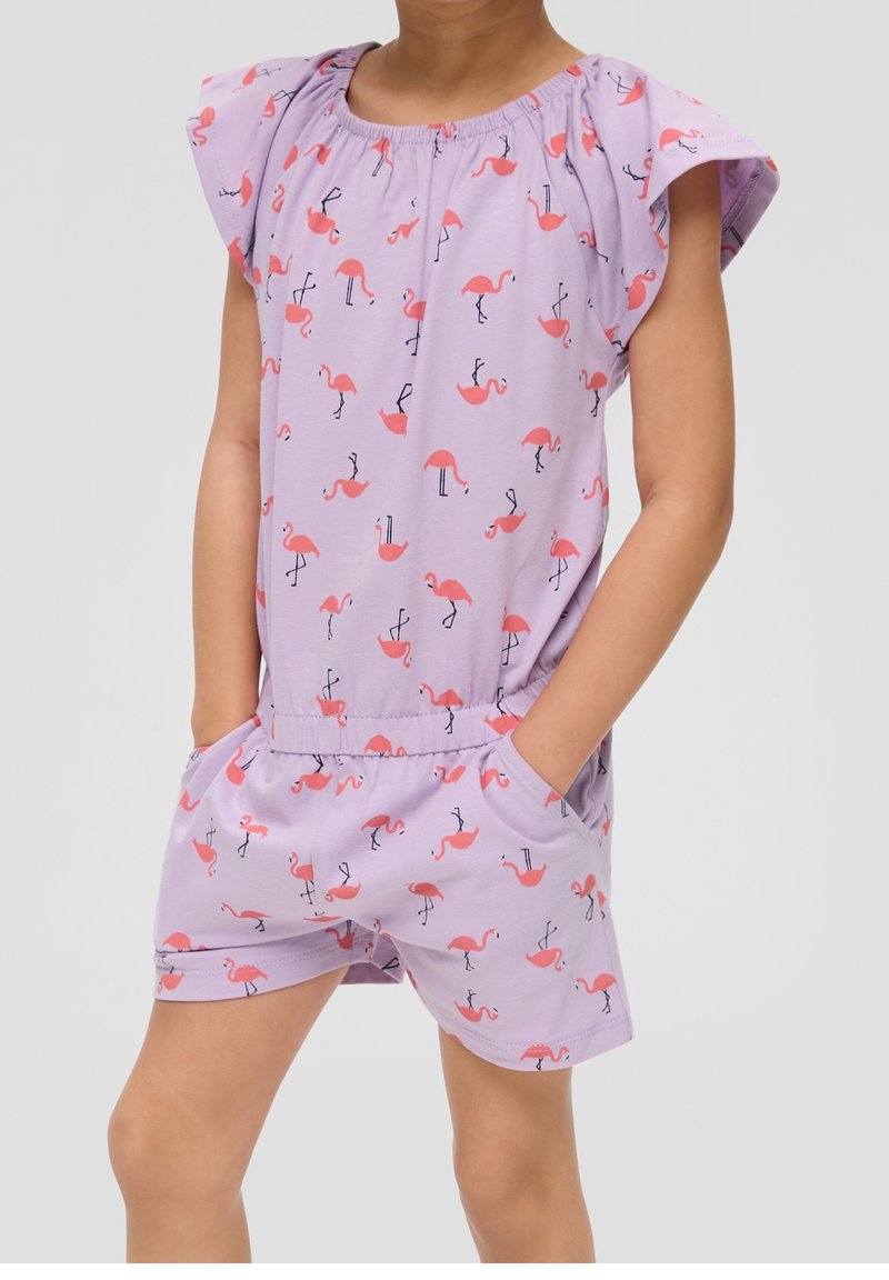 Enfant portant une combinaison lavande imprimée de flamants roses, avec des manches volantées, une taille élastique et les mains dans les poches, sur un fond uni.