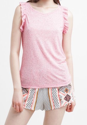 Vrouw die een mouwloze roze top met ruches en een korte broek met geometrische patronen in zwart, oranje en wit draagt.