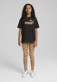 Črna majica s kratkimi rokavi z oranžnim logotipom "PUMA", v kombinaciji z rjavimi legicami z leopardjim vzorcem. Model nosi bele superge. Gladek material in oprijet kroj.