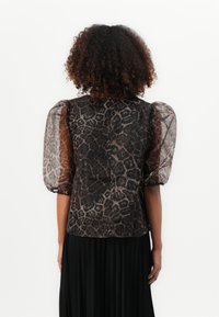 Gjennomsiktig svart bluse med brunt leopardmønster, puffede ermer og rund utringning. Bak har den en knappelukking og jevn tekstur.