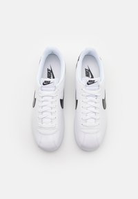 White Nike sneakers featuring a sleek design, smooth leather upper, black swoosh logo, and traditional lacing system.