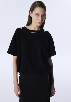 Zwarte oversized sweatshirt met geribde halslijn, met korte mouwen en een gathered onderkant. Wordt gecombineerd met een bijpassende zwarte rok.