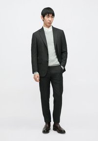 Prugasti crni komplet odijela s uskim hlačama i krojenim sako jaknom preko svijetlosivog džempera, uparen s tamnobrunim kožnim čizmama.