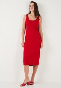 Abito midi rosso aderente con scollatura a cuore e spalline. Tessuto liscio e elastico che si adatta al corpo. Il modello abbina i tacchi rossi coordinati.