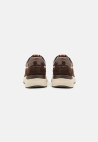 Brune semskede og lædersneakers med rosa accenter, rund form, polstret såle og synlig mærkelogo på bagsiden.