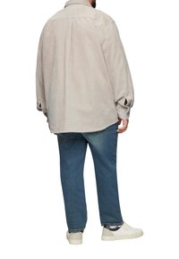 Hellbeige Cordhemd mit lässiger Passform, langen Ärmeln und Rückenfalte, kombiniert mit blauen Jeans und weißen Sneakers.